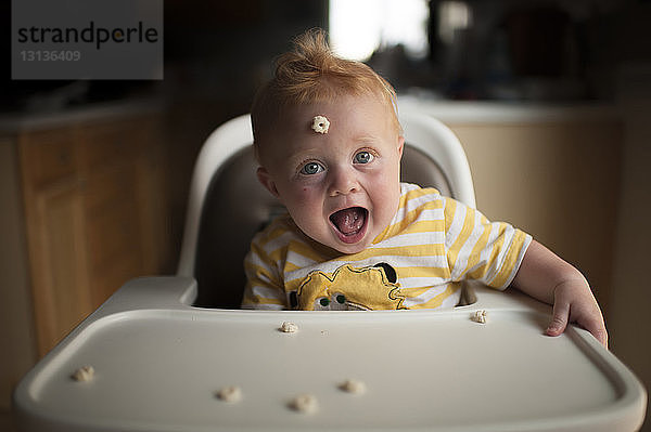 Porträt eines süßen kleinen Jungen  der auf einem Hochstuhl sitzend mit Frühstücksflocken spielt