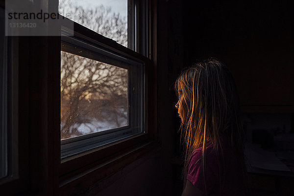 Seitenansicht eines am Fenster sitzenden Mädchens in der Dunkelkammer