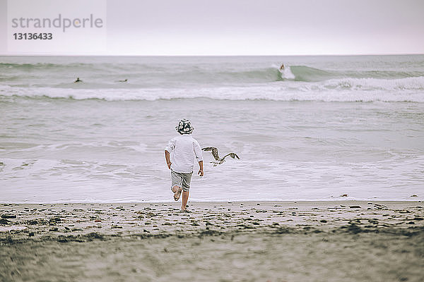 Rückansicht eines Jungen  der am Strand auf Sand läuft