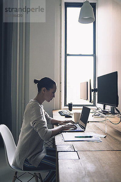Seitenansicht einer Geschäftsfrau  die einen Laptop benutzt  während sie im Büro am Schreibtisch sitzt