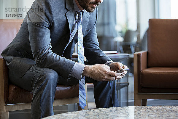 Mittelsektion eines Geschäftsmannes  der ein Smartphone auf einem Sessel im Büro benutzt