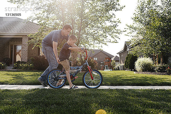 Vater hilft Sohn beim Fahrradfahren auf Straße gegen Himmel