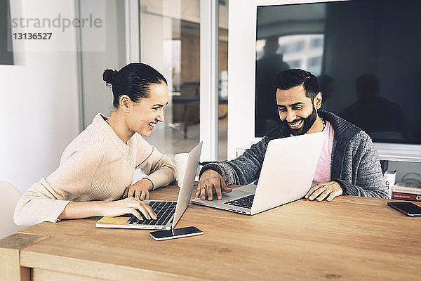 Lächelnde Geschäftsleute  die im Büro sitzen und auf Laptops schauen