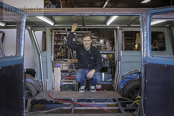 Porträt eines lächelnden  selbstbewussten Ingenieurs  der in einem beschädigten Lieferwagen in der Fabrik kauert