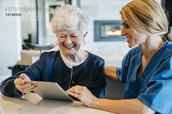 Glückliche ältere Frau  die einen Tablet-Computer mit einer häuslichen Pflegekraft benutzt