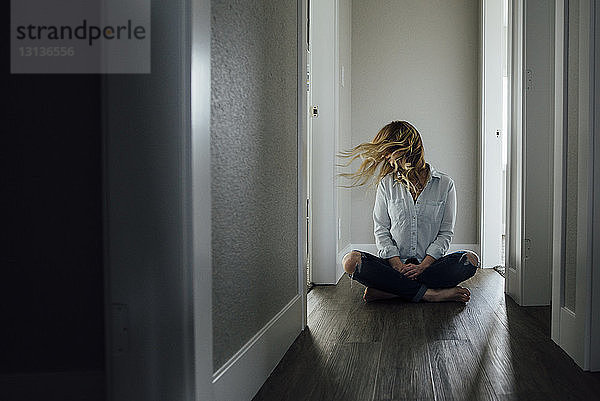 Frau in voller Länge  die auf dem Boden sitzend auf dem Flur zu Hause mit den Haaren wackelt