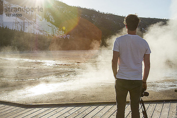 Rückansicht eines Wanderers mit Blick auf den Dampf  der aus einer heißen Quelle im Yellowstone-Nationalpark austritt
