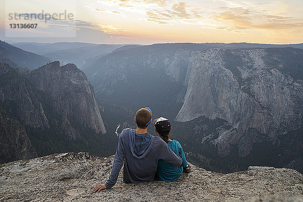 Rückansicht eines Paares  das bei Sonnenuntergang auf einem Berg sitzt
