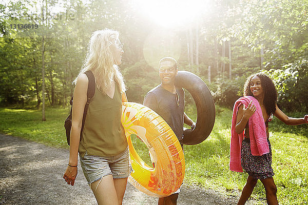 Fröhliche Freunde mit aufblasbaren Ringen beim Spaziergang auf einer Straße im Wald im Sommer