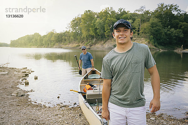 Porträt eines jungen Mannes  der mit einem Freund ein Boot in Richtung Seeufer schiebt