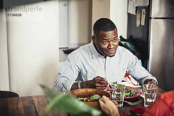Lächelnder Mann im Gespräch mit dem Partner beim Salatessen am Esstisch
