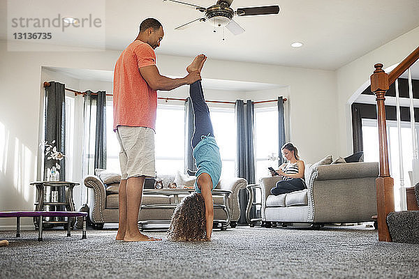 Vater hilft Tochter beim Handstand im Wohnzimmer zu Hause