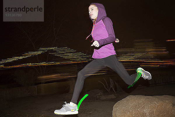 Seitenansicht einer Joggerin mit Kapuze beim nächtlichen Laufen auf dem Feld