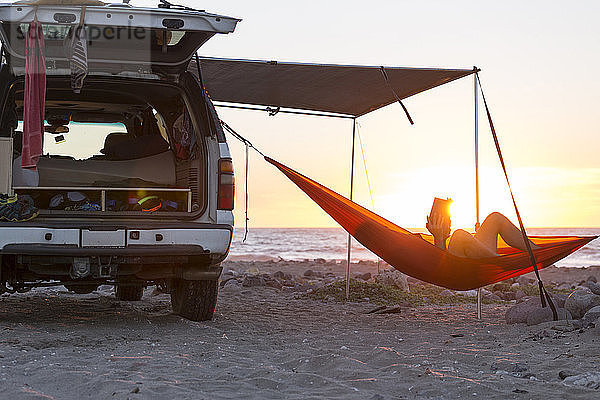 Mann entspannt sich bei Sonnenuntergang in Hängematte am Strand