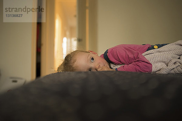 Seitenansicht eines nachdenklichen Mädchens  das im Bett liegend wegschaut