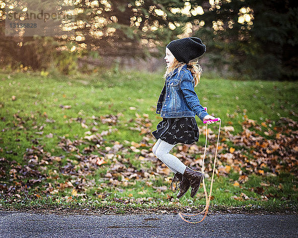 Seitenansicht eines Mädchens  das im Herbst auf einem Fußweg im Park Seil springt