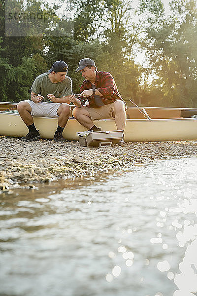 Männliche Freunde justieren Angelruten  während sie auf einem Boot am See sitzen