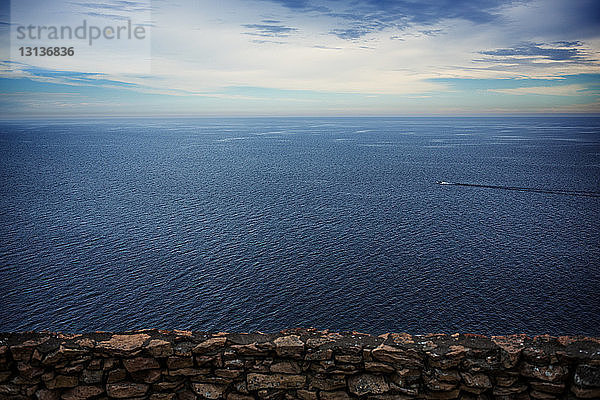 Zurückhaltende Steinmauer mit Blick auf die Meereslandschaft gegen bewölkten Himmel