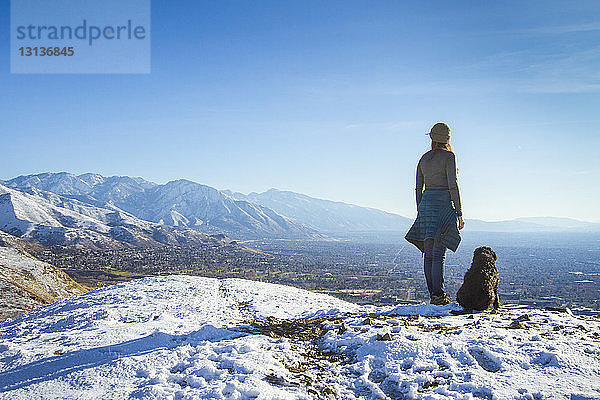 Rückansicht einer Frau mit Hund  die im Winter auf einem Berg gegen den Himmel steht