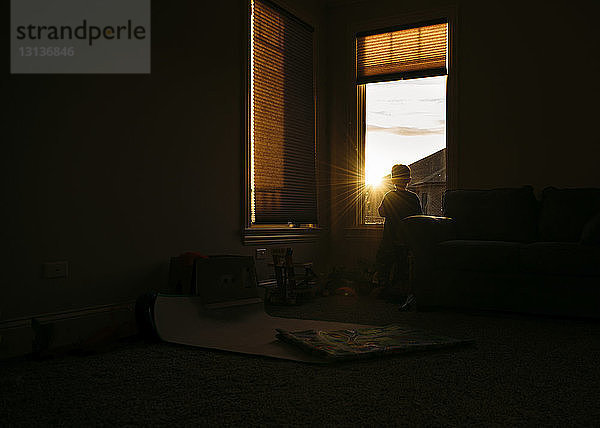 Silhouette eines Jungen  der zu Hause durchs Fenster schaut