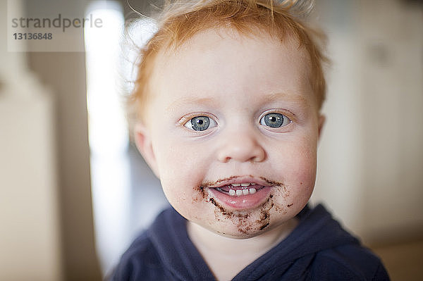 Porträt eines süßen kleinen Jungen  dem zu Hause das Essen um den Mund herumgeworfen wird