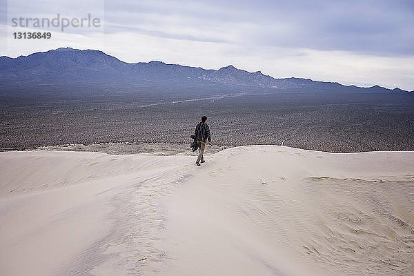 Rückansicht in voller Länge eines Mannes  der auf einer Sanddüne in der Wüste geht