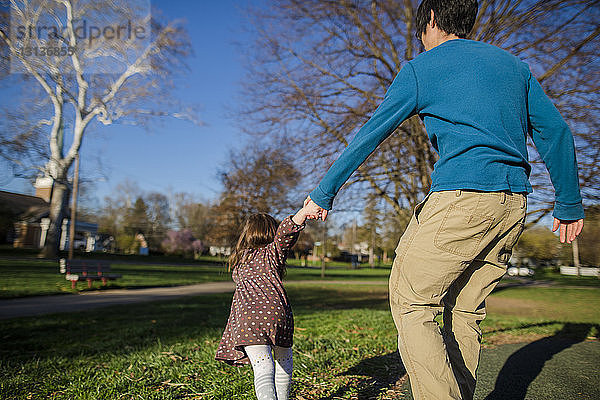 Rückansicht einer Tochter  die den Vater mit den Händen im Park an sich zieht