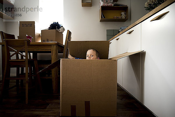 Porträt eines verspielten Jungen  der zu Hause in einem Pappkarton sitzt