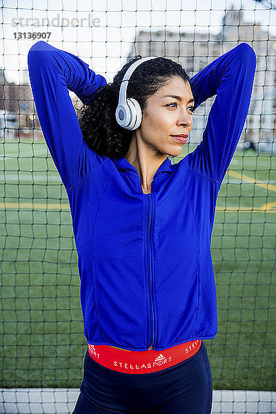 Selbstbewusste Sportlerin mit erhobenen Armen  die Musik hört  während sie am Netz steht