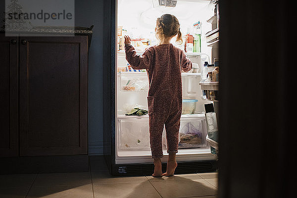 Rückansicht eines Mädchens  das zu Hause am Kühlschrank steht