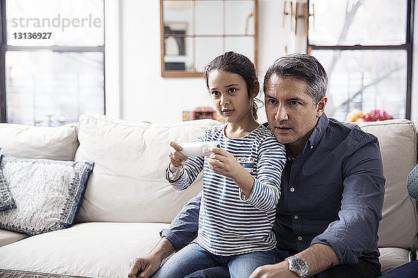 Mädchen spielt Videospiel  während sie mit dem Vater zu Hause sitzt