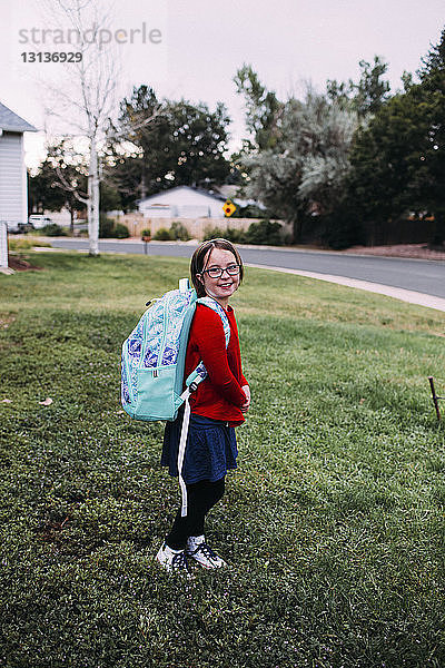 Porträt eines auf dem Rasen stehenden Mädchens mit Rucksack