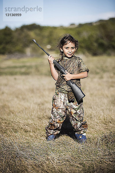 Porträt eines selbstbewussten Mädchens mit Gewehr in der Hand auf einem Grasfeld