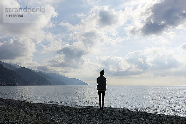 Silhouette einer am Ufer stehenden Frau am Strand