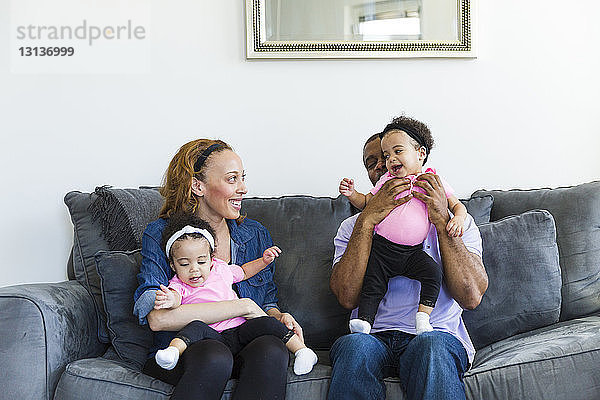 Glückliche Eltern spielen mit ihren Töchtern  während sie auf dem Sofa sitzen