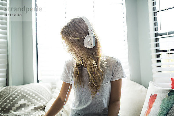 Frau hört Musik über Kopfhörer  während sie auf einem Fensterplatz in einer Nische sitzt