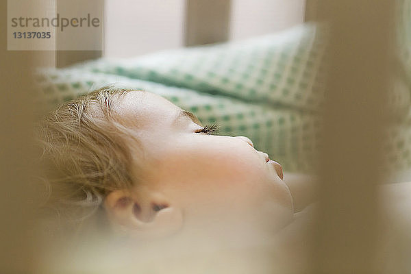 Nahaufnahme eines süßen  in einem Kinderbett schlafenden Mädchens durch ein Geländer zu Hause gesehen