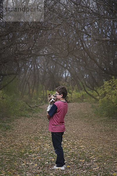 Junge trägt Hund  während er auf Grasfeld im Park steht