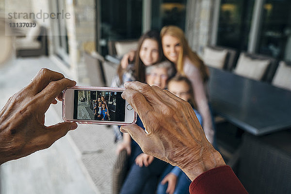 Abgetrennte Hände eines älteren Mannes fotografieren Familie durch ein Smartphone auf der Veranda
