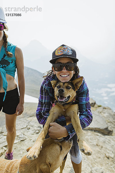 Porträt einer Frau  die einen Hund umarmt  während sie bei einem Freund auf einem Berg vor klarem Himmel steht