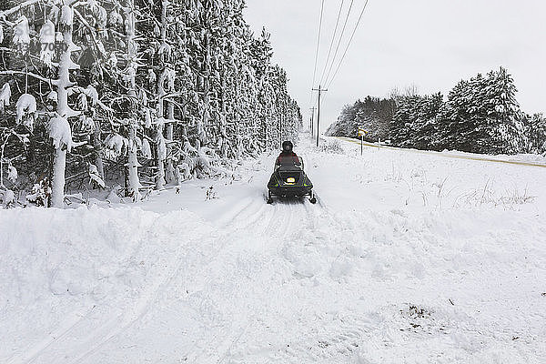 Rückansicht eines Teenagers  der auf einem schneebedeckten Feld gegen den Himmel im Wald Quad fährt