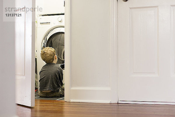 Junge schaut durch die Tür auf Waschmaschine