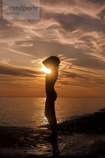 Seitenansicht der Silhouette einer sinnlichen Frau  die bei Sonnenuntergang am Strand steht