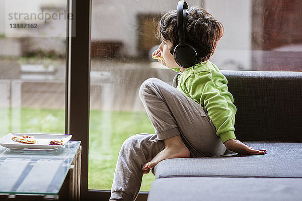 An einen Jungen gedacht  der Musik hört  während er zu Hause auf dem Sofa am Fenster isst