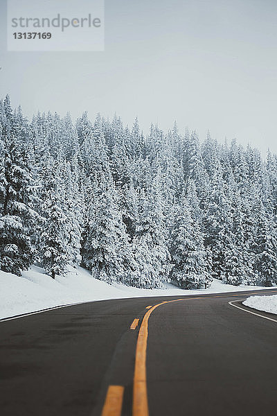 Leere Straße inmitten schneebedeckter Bäume im Wald gegen den Himmel