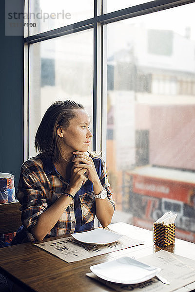 Nachdenkliche Frau  die durch das Fenster schaut  während sie im Café sitzt