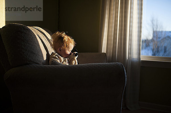 Kleiner Junge spielt mit Spielzeug  während er bei Sonnenuntergang zu Hause auf der Couch sitzt