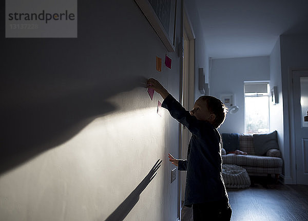 Seitenansicht eines Jungen  der zu Hause Haftnotizen an die Wand klebt