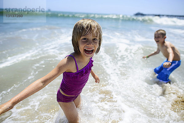 Porträt eines glücklichen Mädchens  das mit seinem Bruder im Meer am Strand von Oceanside spielt