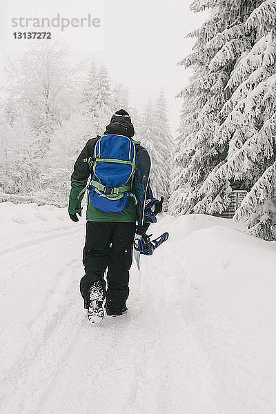 Rückansicht eines Mannes mit Snowboard  der auf einem schneebedeckten Feld läuft